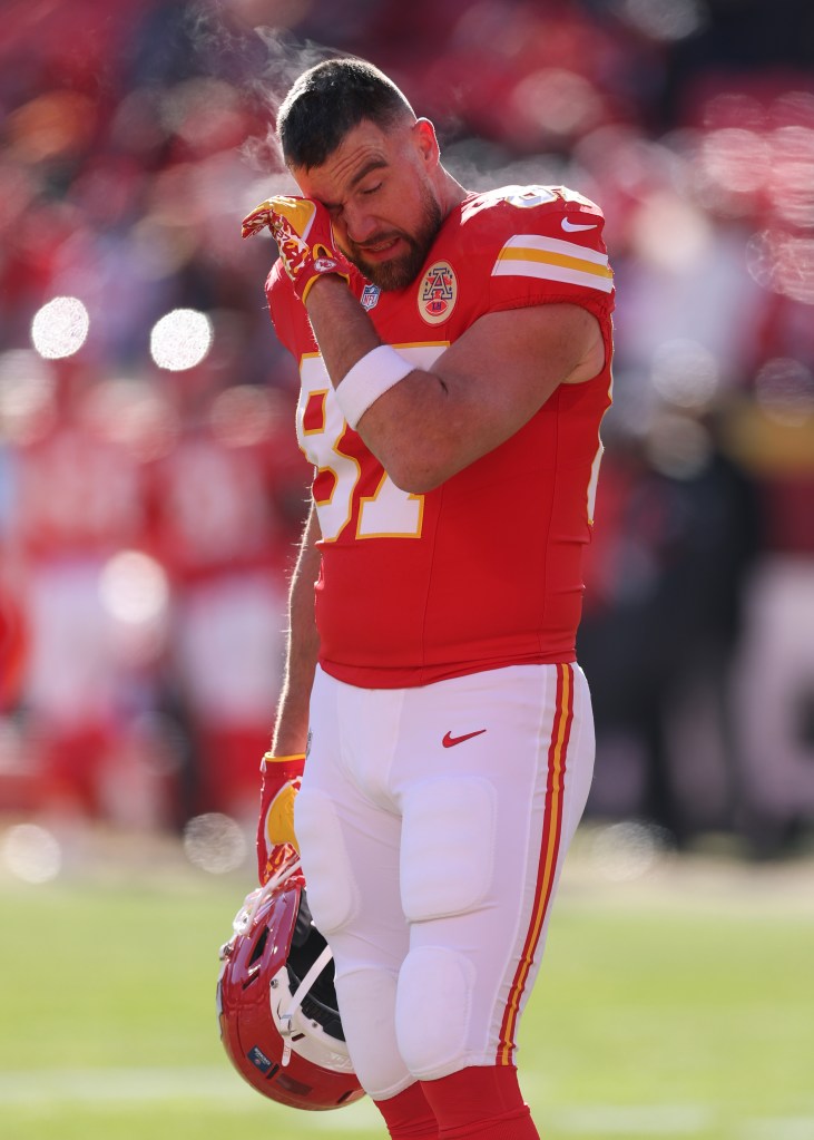 Kansas City Chiefs player Travis Kelce warming up, wiping his face, with his breath visible in the cold air.