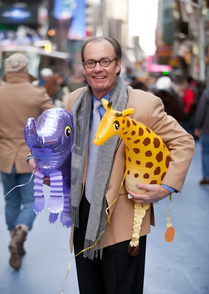 Treb Heining holds an inflated purple elephant and yellow giraffe in Times Square.