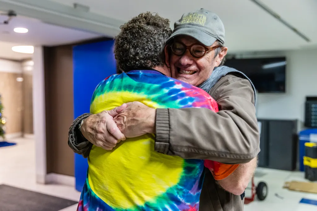 Treb Heining on the left, wearing a brown jacket, greets an old friend with a hug.