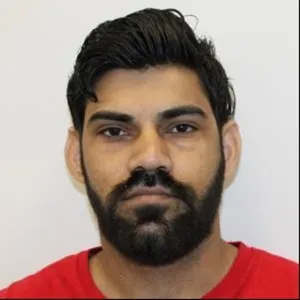 Mugshot of a man with dark hair and beard, wearing a red shirt.