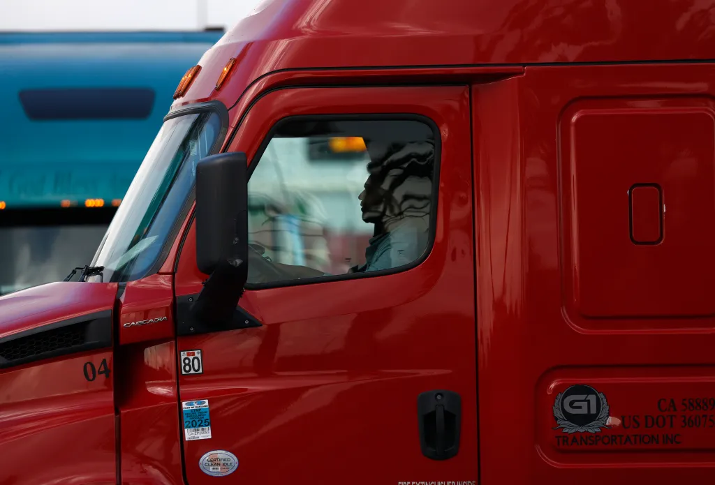 A person driving a red commercial truck at the Port of Oakland.
