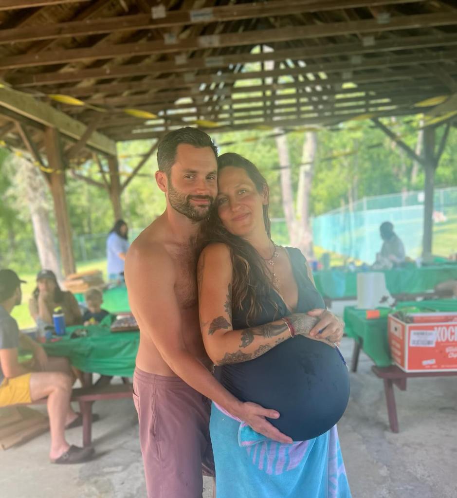Domino Kirke and Penn Badgley, with Domino holding her pregnant belly, standing under a gazebo.