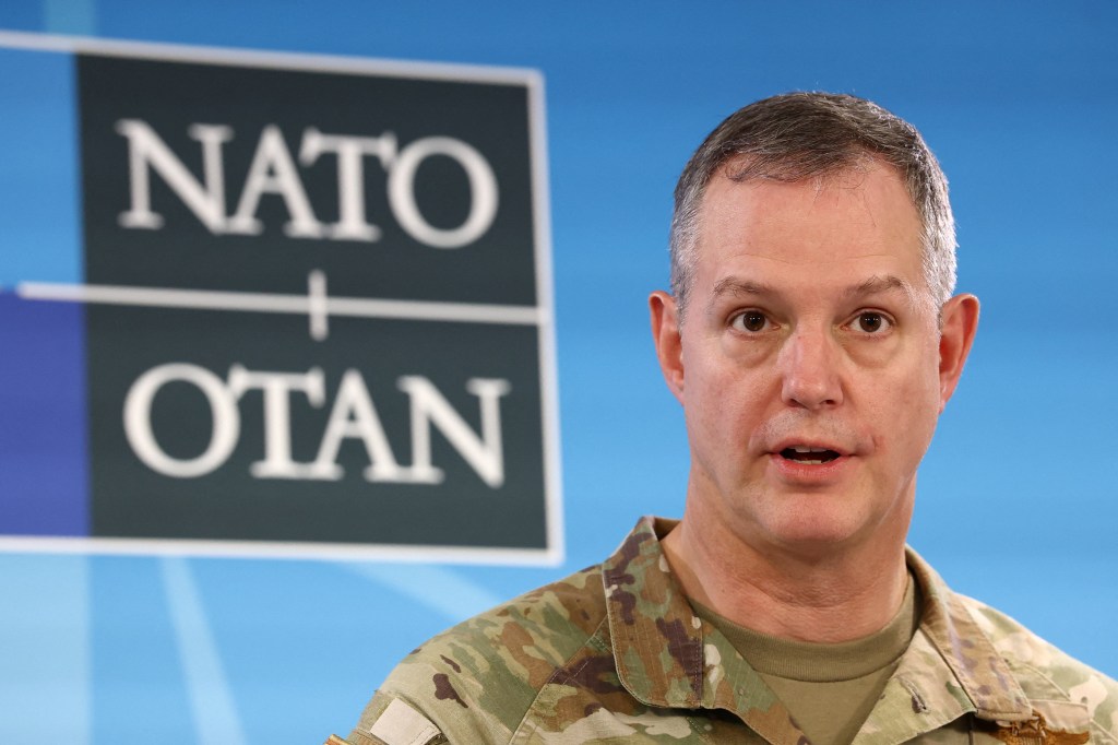General Alexus Grynkewich speaking at a press conference with the NATO logo in the background.
