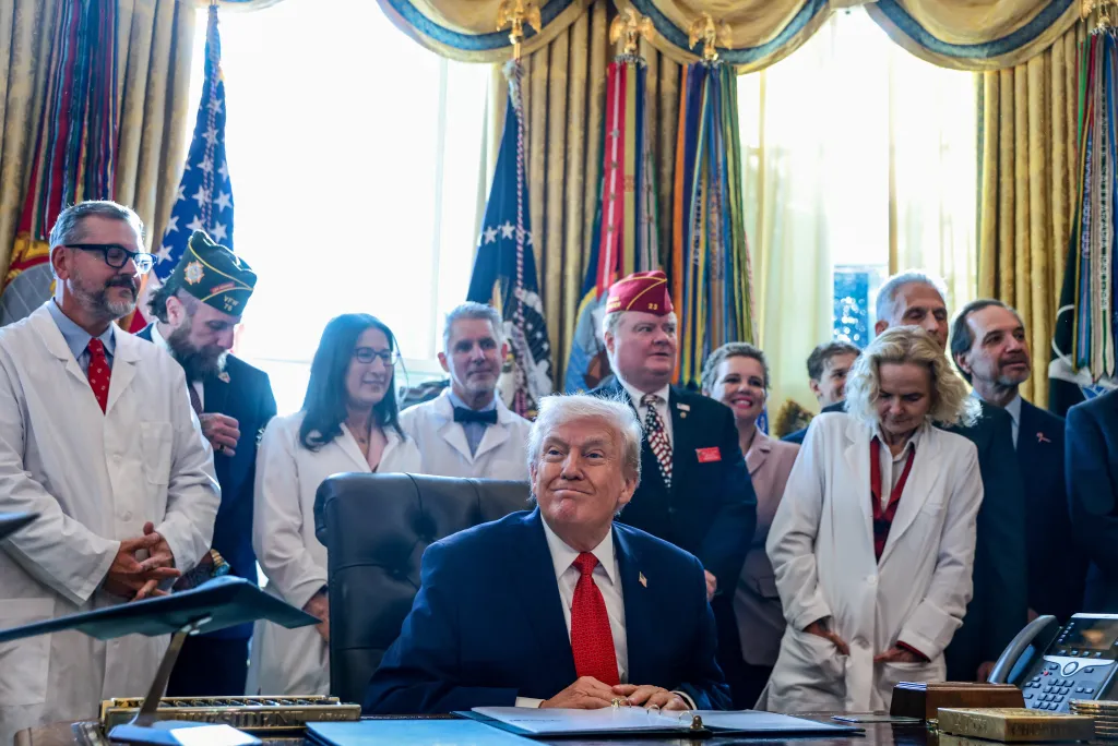 U.S. President Donald Trump in the Oval Office, surrounded by people, signs an executive order.