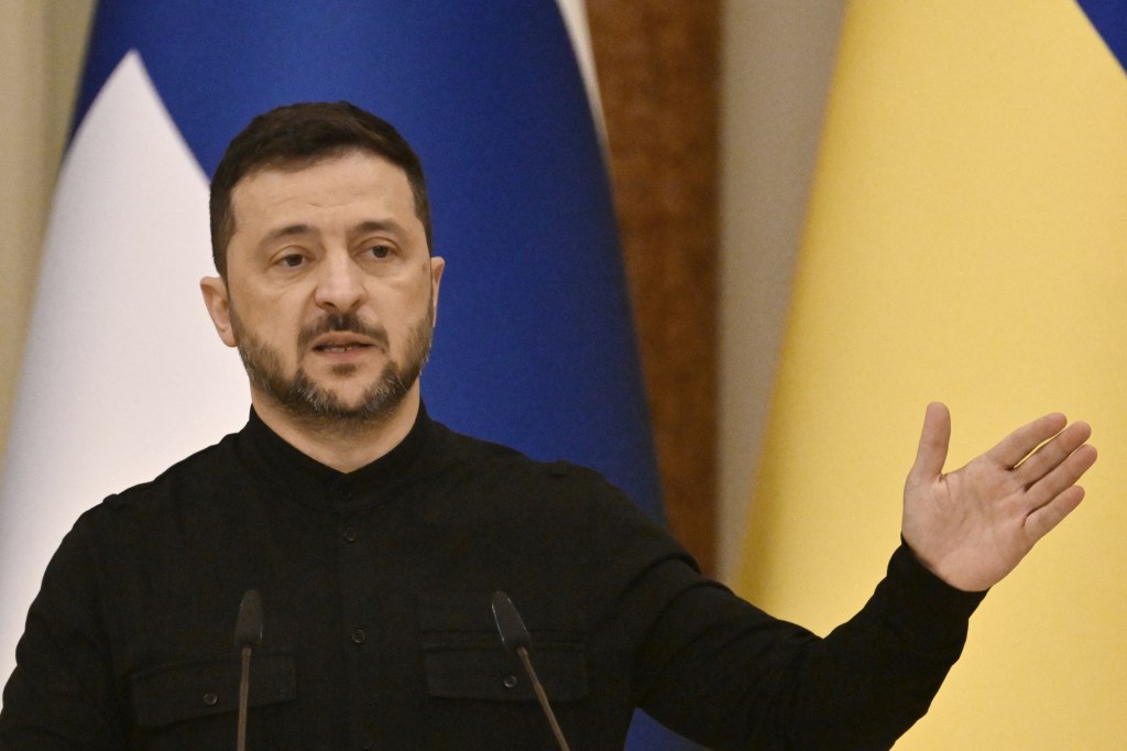 Ukrainian President Volodymyr Zelensky speaking at a press conference with the Finnish flag and Ukrainian flag in the background.