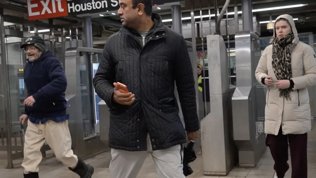 An unidentified fare evader, left, tailgates a paying straphanger to pass through the new glass subway turnstiles at the Broadway Lafayette station.