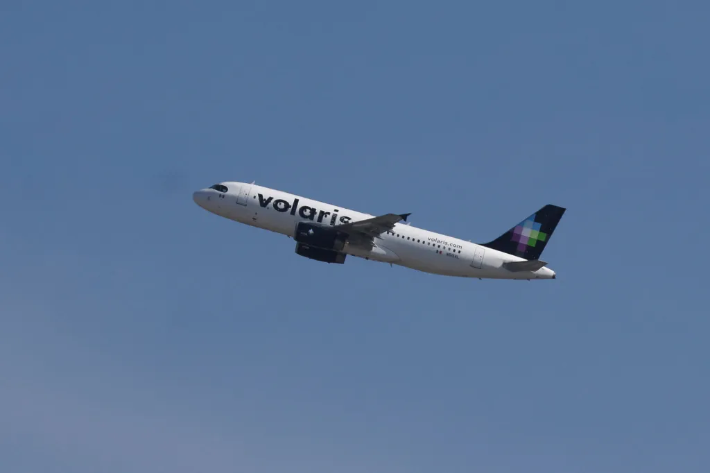 A Volaris airplane takes off from Felipe Angeles International Airport (AIFA) against a clear blue sky.