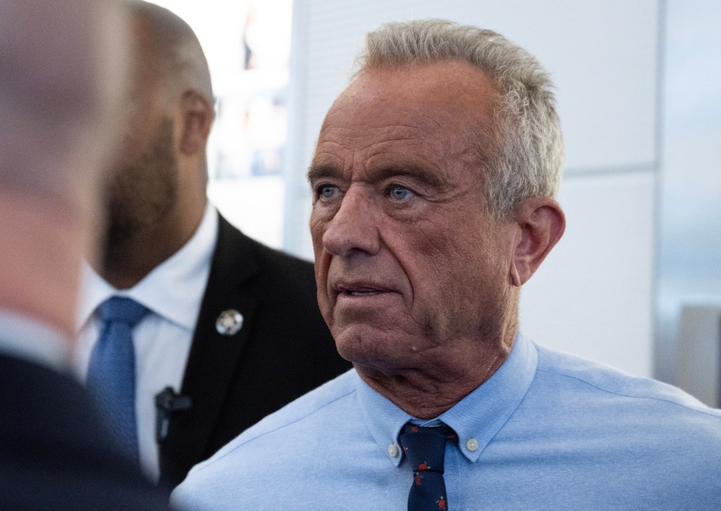 Robert F. Kennedy, Jr. looking intently forward while a blurred figure stands behind him.