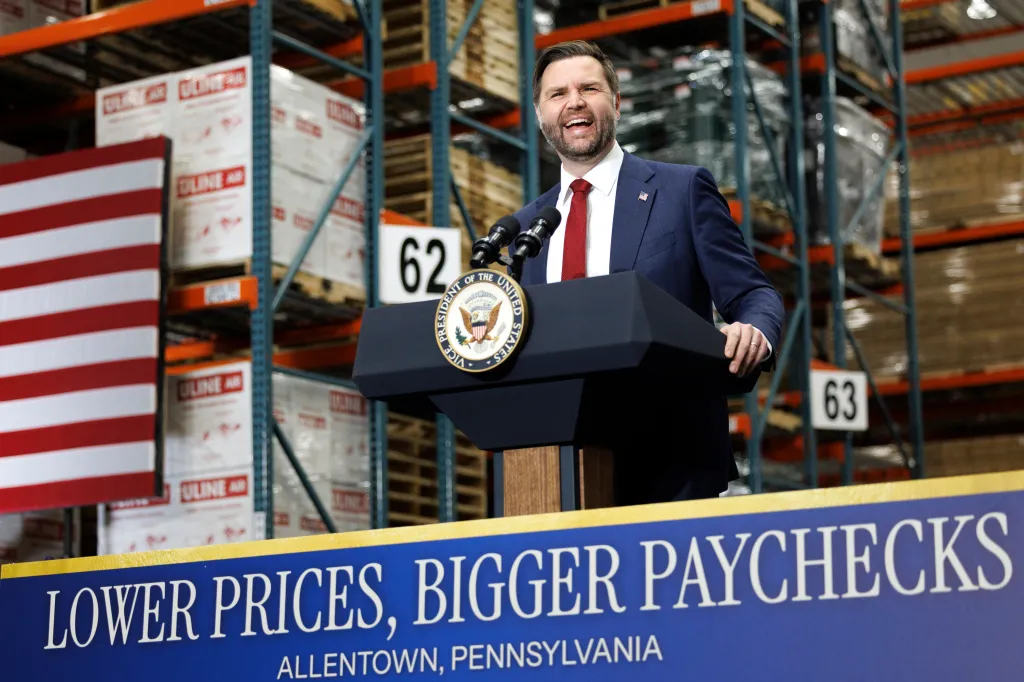 JD Vance speaks at a podium in a warehouse with a sign reading 