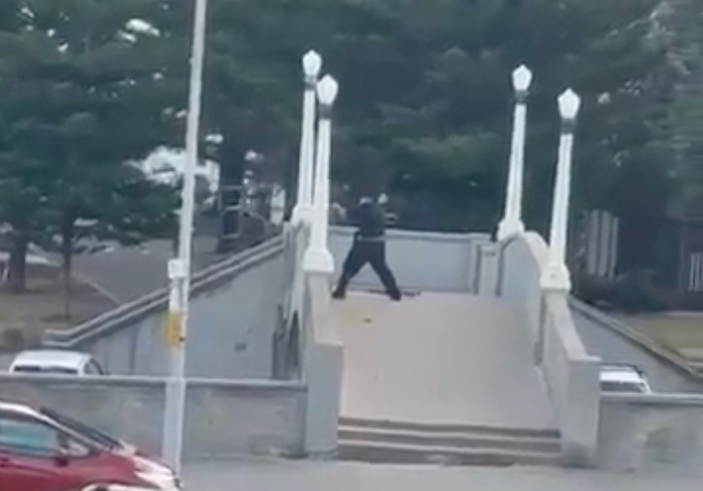 A gunman on a bridge over Bondi Beach, holding a weapon.