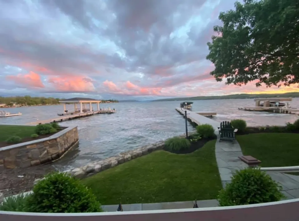 View of a New York lake with a sunset sky over a dock and gazebo.