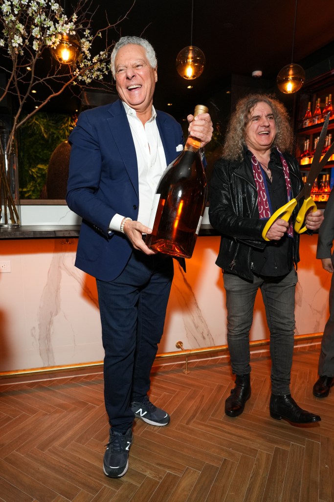 Vittorio Assaf holding a large bottle of liquor and a guest holding oversized scissors.