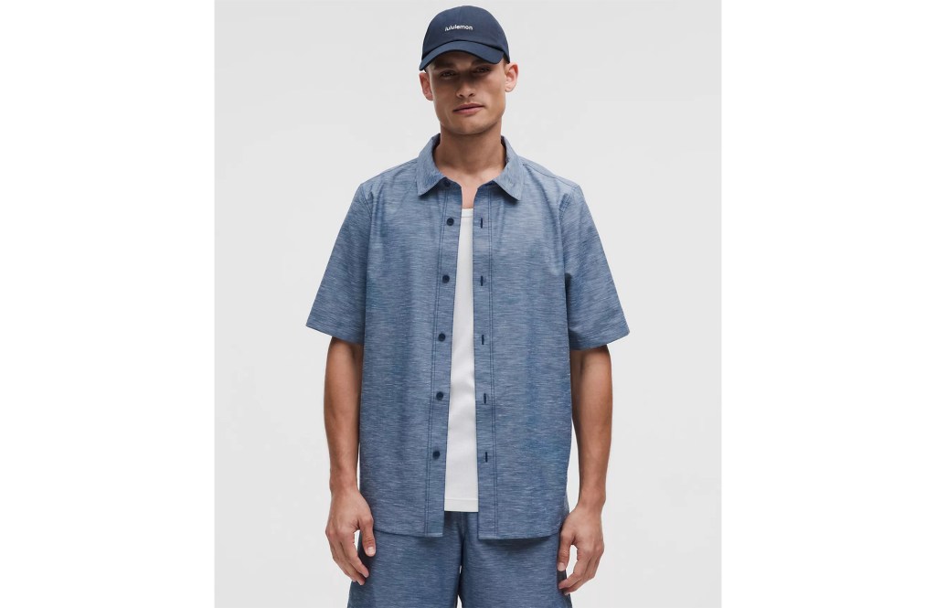 Man wearing a blue short-sleeved shirt, white undershirt, blue shorts, and a blue baseball cap.