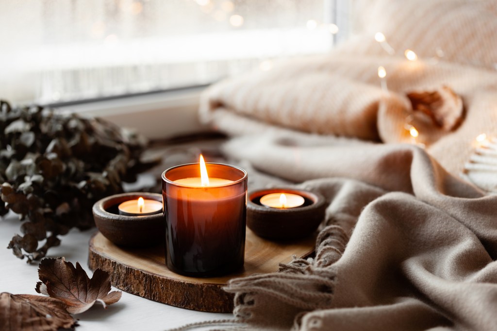 Warm and cozy window arrangement with candles, a blanket, and string lights.