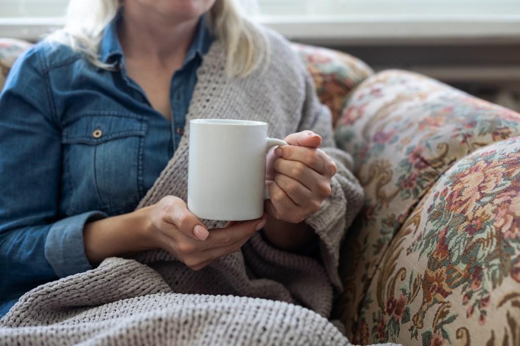 Woman holding a warm cup of coffee while wrapped in a blanket.