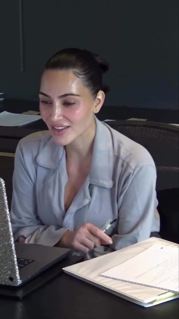 Kim Kardashian looking at a laptop and holding a pen.