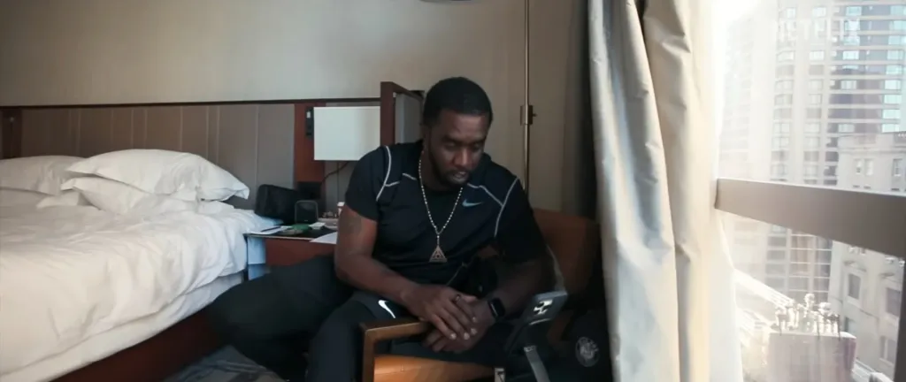 Sean 'Diddy' Combs sitting in a hotel room with city views outside the window.