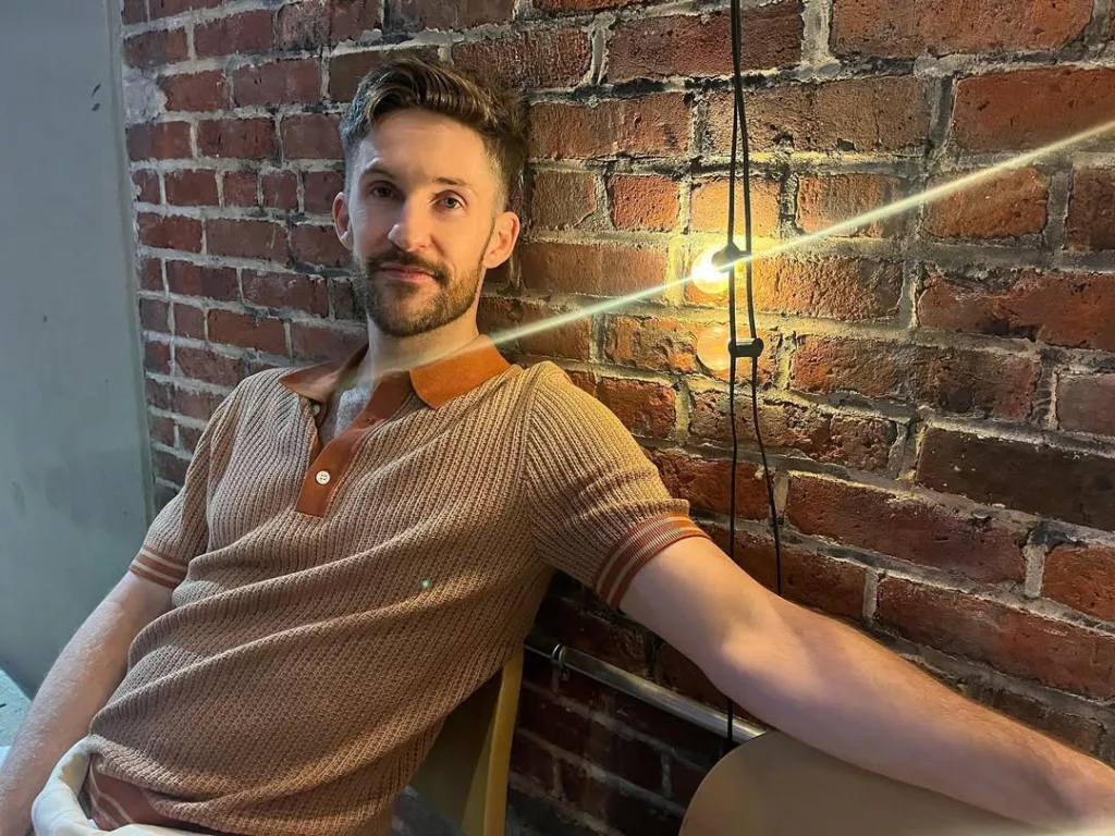 Jimmy Fowlie sitting in front of a brick wall with a light bulb next to him.