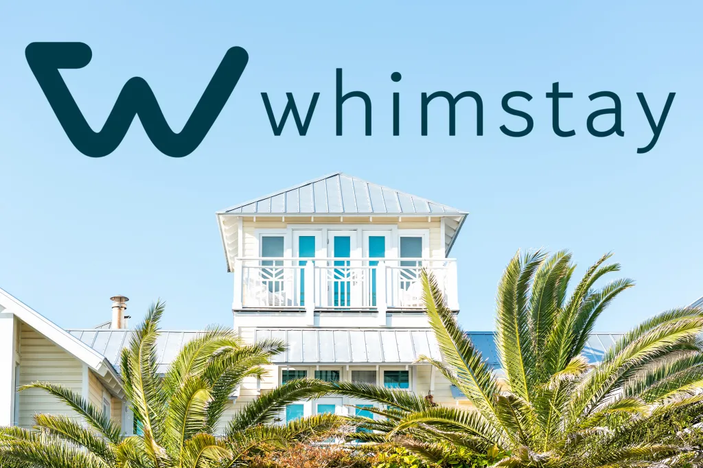 Whimstay logo above a white building with balconies and palm trees.