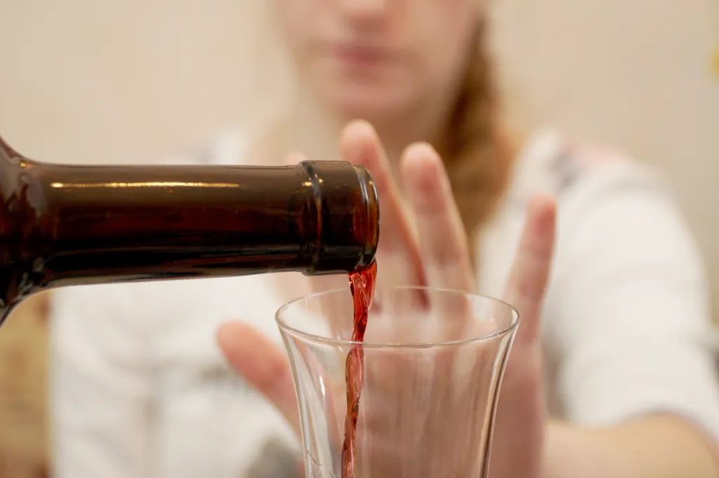 A young girl refusing a glass of wine being poured from a bottle.