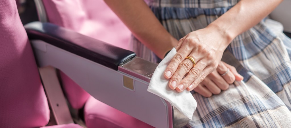 Woman cleaning an airplane seat armrest with a wet wipe.