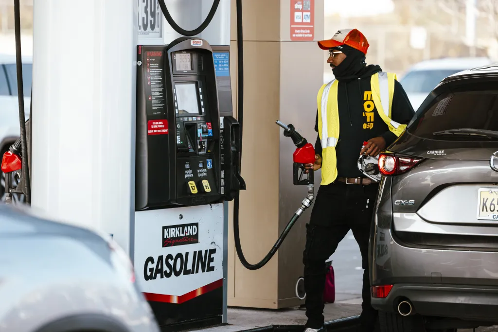 A worker at a Costco gas station in Bayonne, New Jersey, is holding a gas pump while standing next to a car.