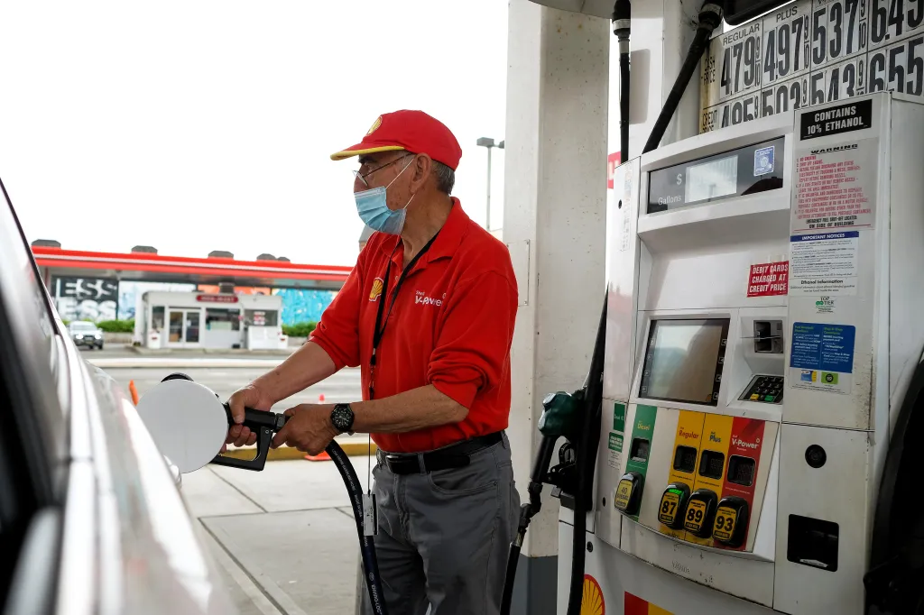 A worker wearing a red shirt and face mask fills a car with gas at a Shell station.