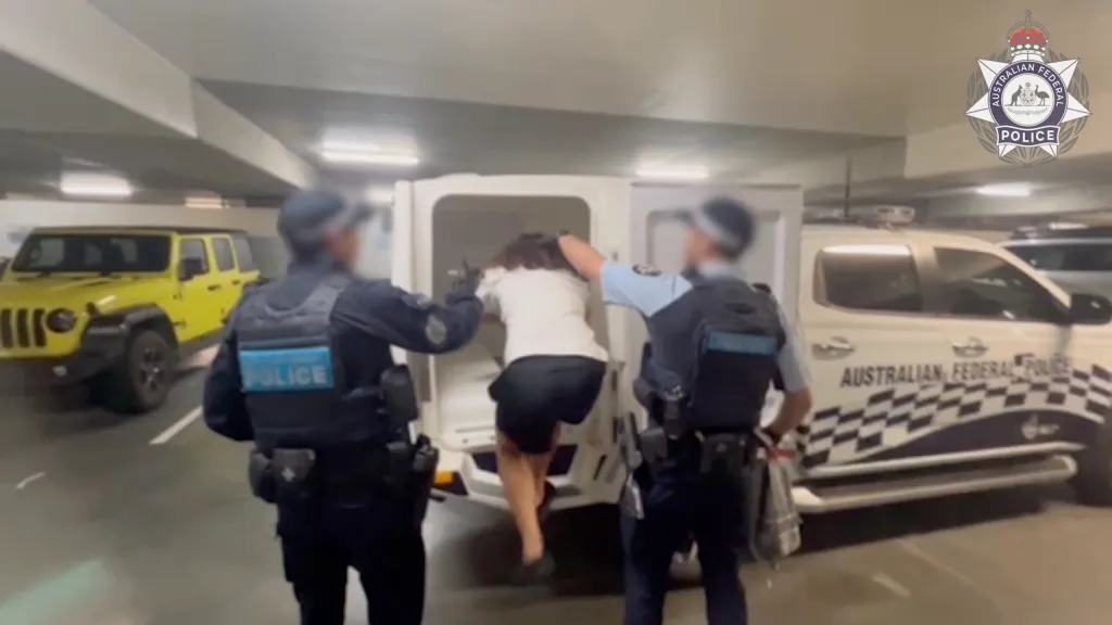 Australian Federal Police officers escorting a man into a police vehicle.