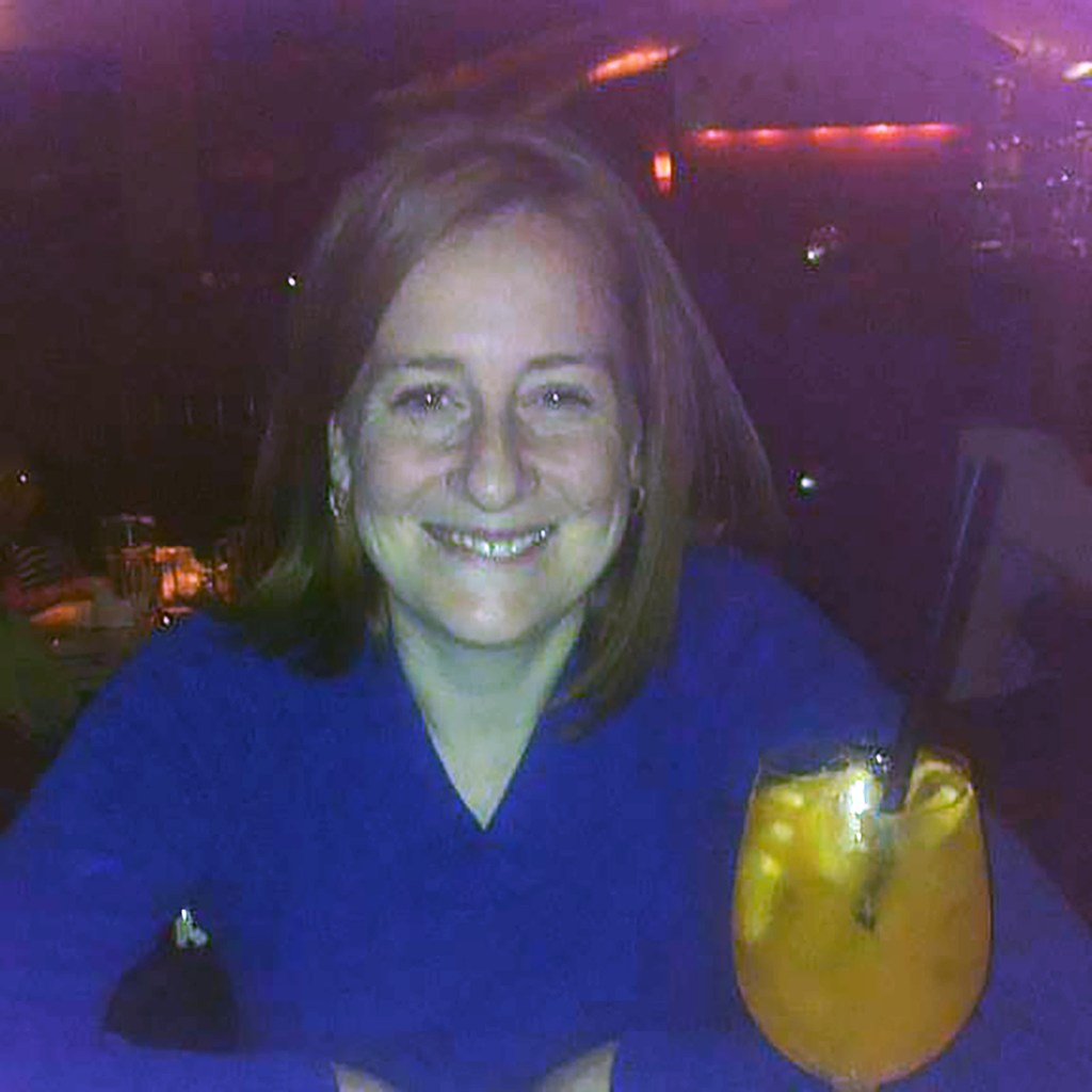 Kerri Aherne, the Macy's stabbing suspect, smiling while sitting at a table with an alcoholic drink.