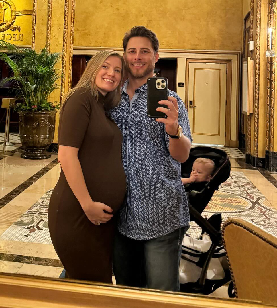 Pregnant Madlyn Ballatori and Colby Kissinger pose in a large room. 