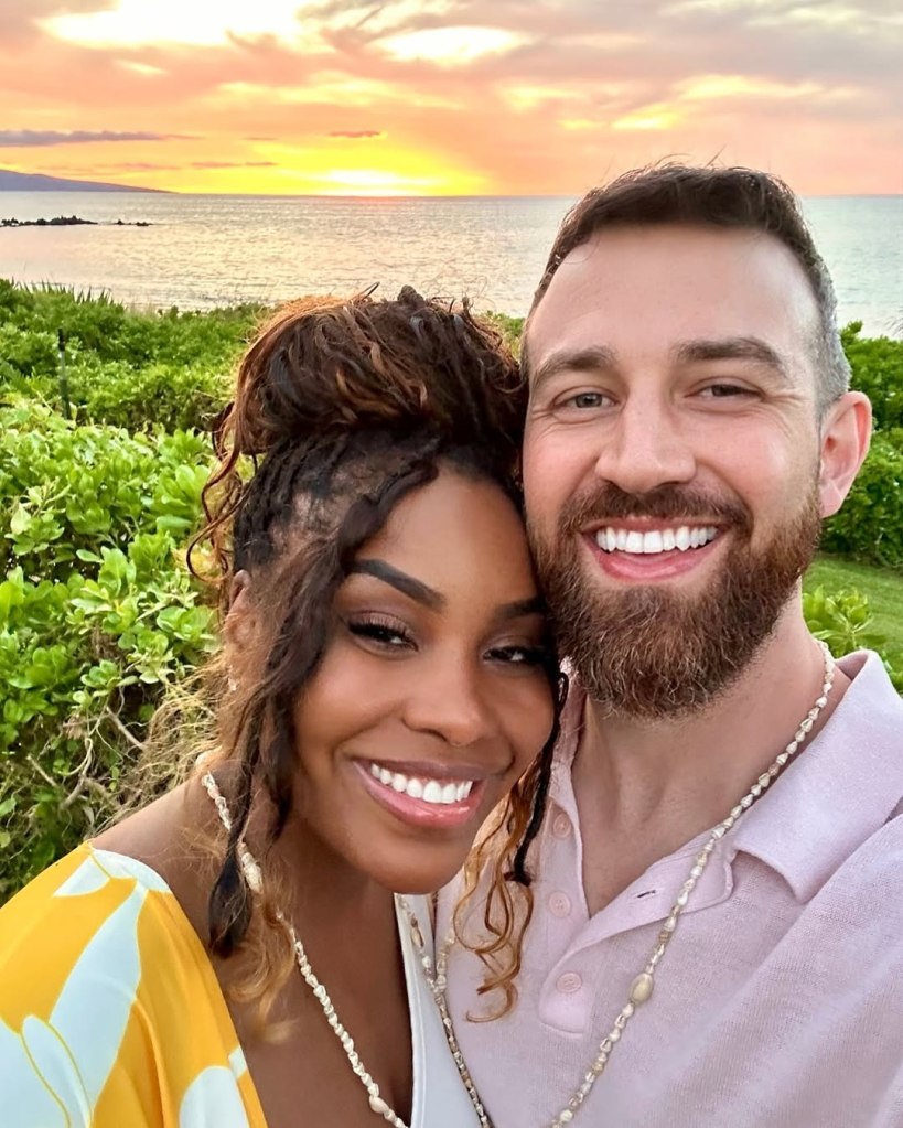 Lauren and Cameron Hamilton posing for a photo with a sunset over the ocean in the background.