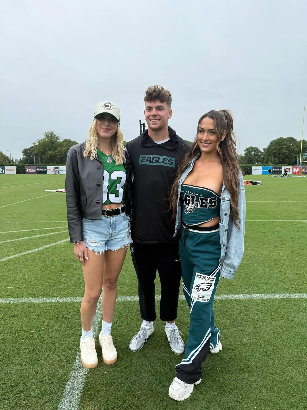 Nikki Bella and Cooper DeJean pose on a football field with another woman.