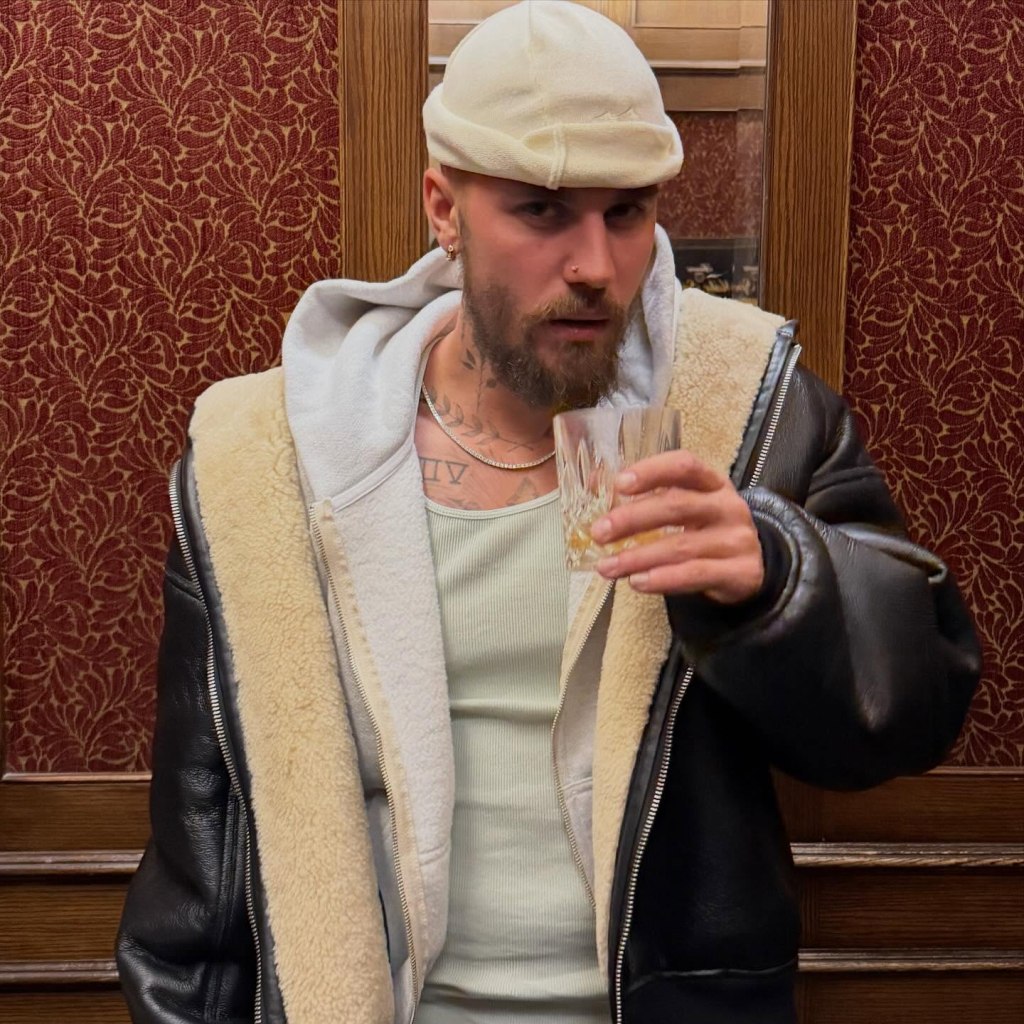 Justin Bieber holding a drink in a leather jacket and beanie.