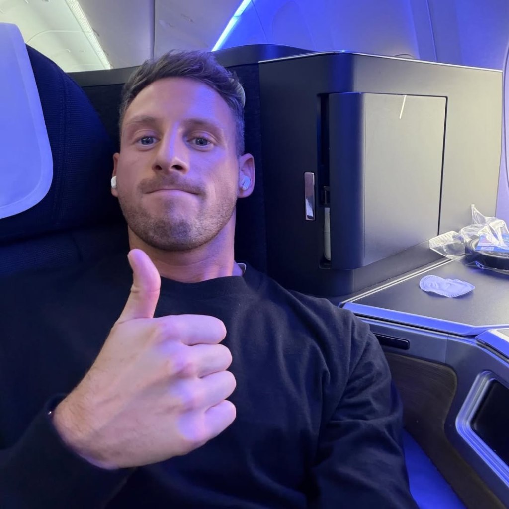Fraser Olender giving a thumbs-up in an airplane seat.