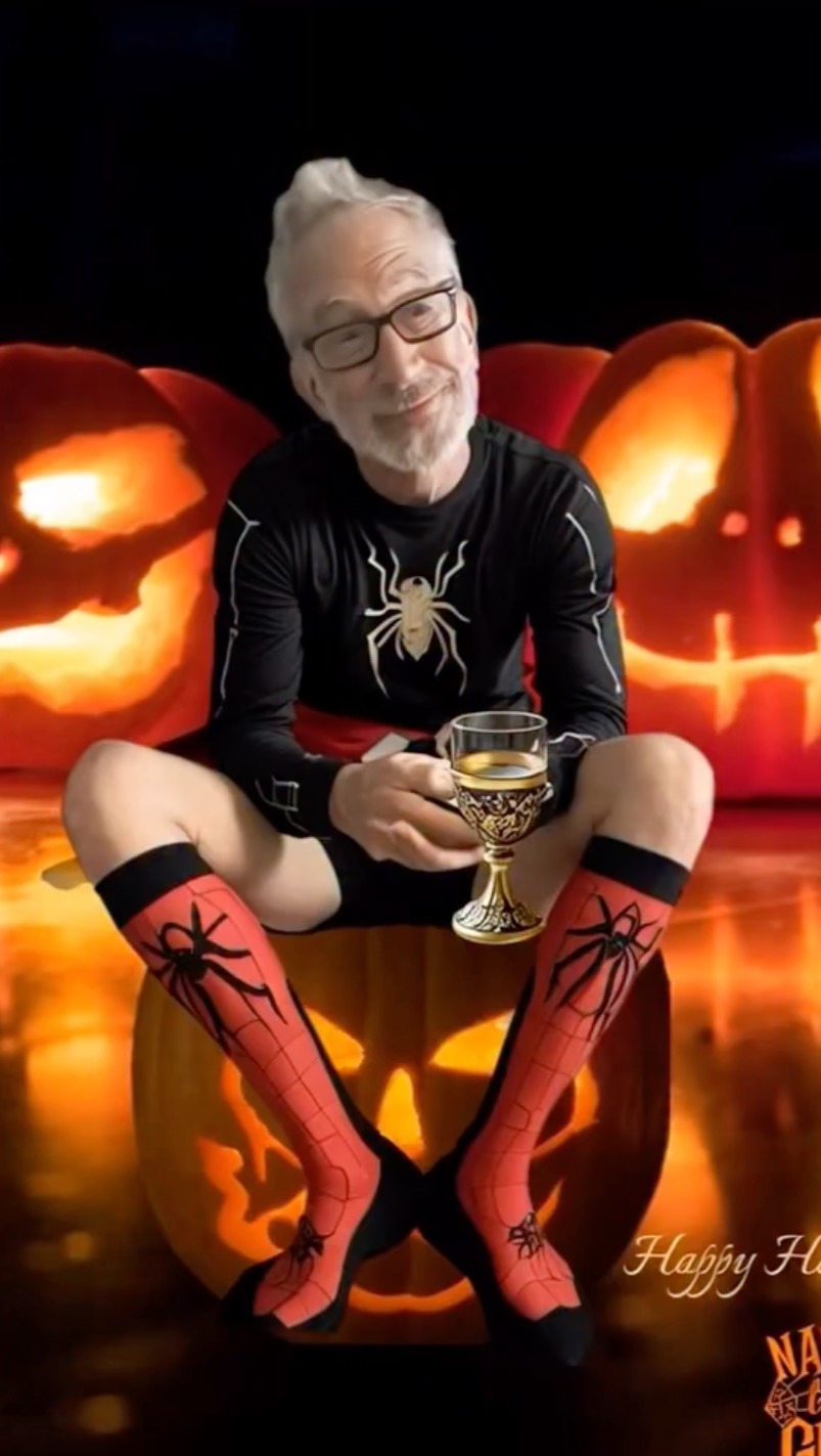 Andy Dick dressed as Spider-Man with socks and a shirt, holding a goblet, sitting on a carved pumpkin.