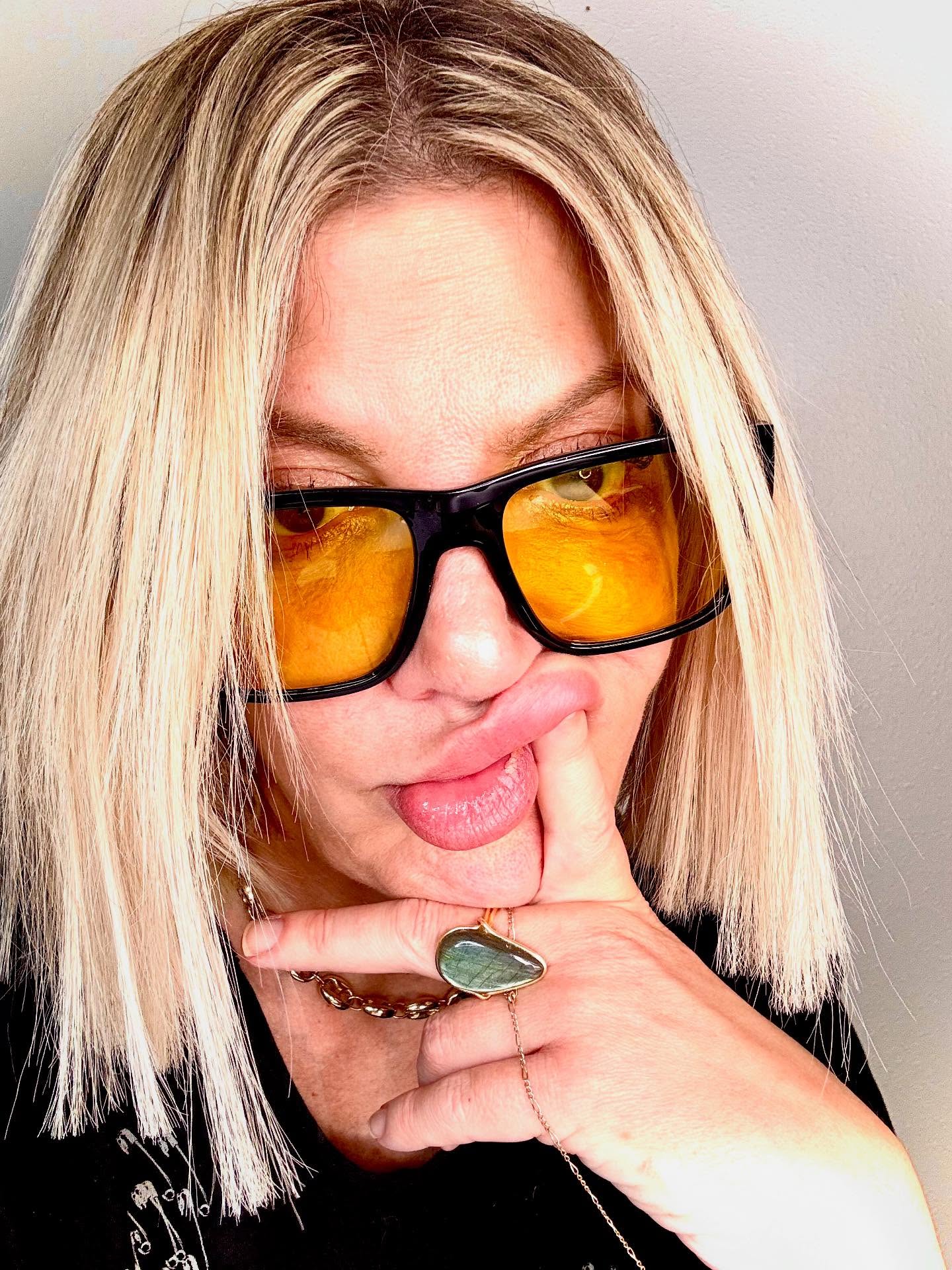 Tori Spelling in yellow-tinted sunglasses, touching her chin.