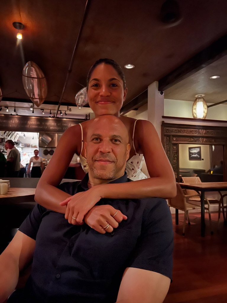 Cory Booker and Alexis in a restaurant, with Alexis embracing Cory from behind.