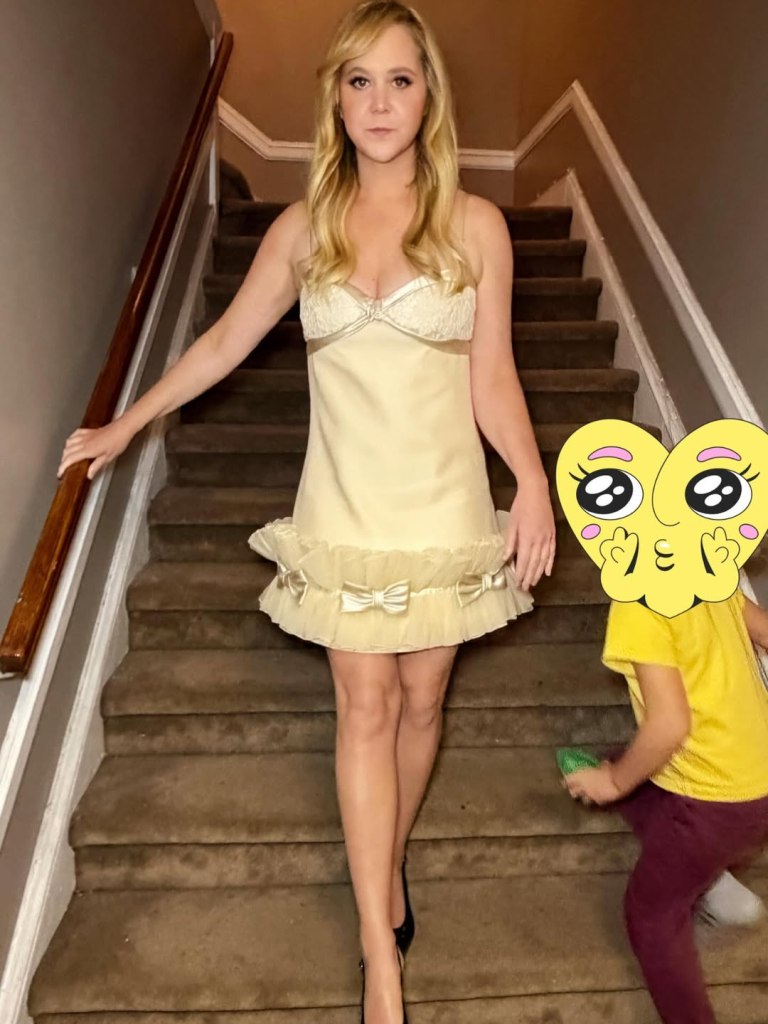 Amy Schumer, in a yellow mini dress, posing on a staircase. Her son wears a yellow t-shirt and burgundy pants.