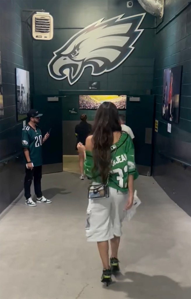 Nikki Bella walking through a corridor with the Philadelphia Eagles logo on the wall.