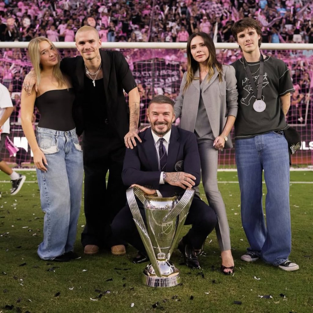 David Beckham with his family and a trophy on a soccer field.