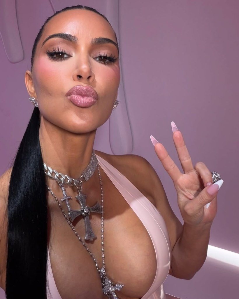 Kim Kardashian with a kissy face, making a peace sign with her left hand.