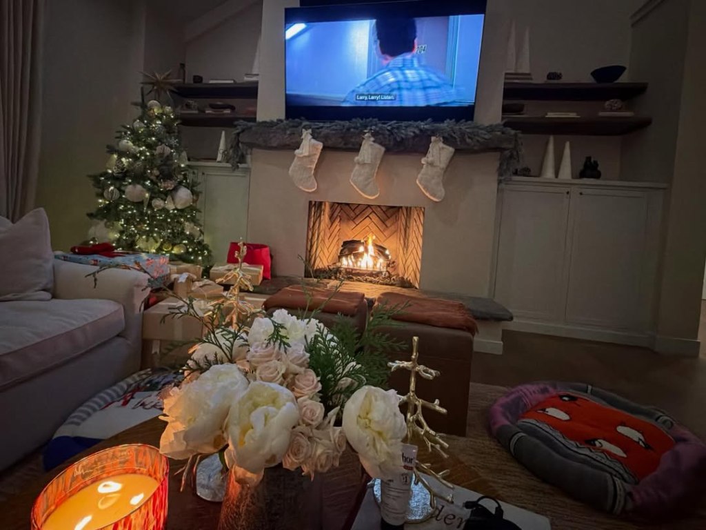 A cozy living room decorated for Christmas with a lit tree, fireplace, and presents.