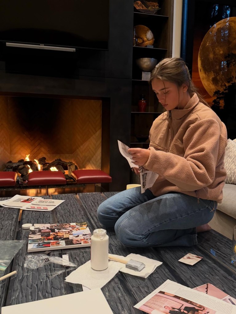 A young woman sitting cross-legged on a coffee table with various items for arts and crafts.
