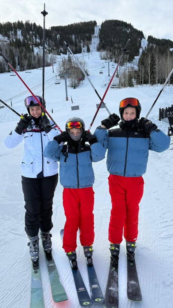 Three children in ski gear standing on skis with poles on a snowy mountain.