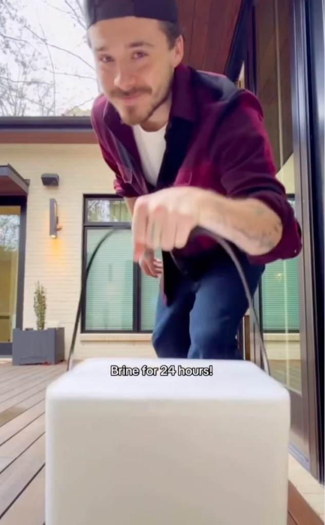 Brooklyn Beckham holds up a long, dark object above a white container with the text 