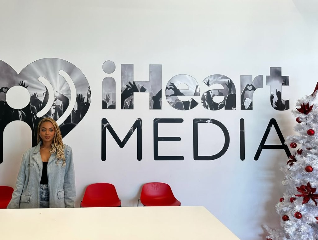 Mickey Lee posing in front of the iHeartMedia logo.