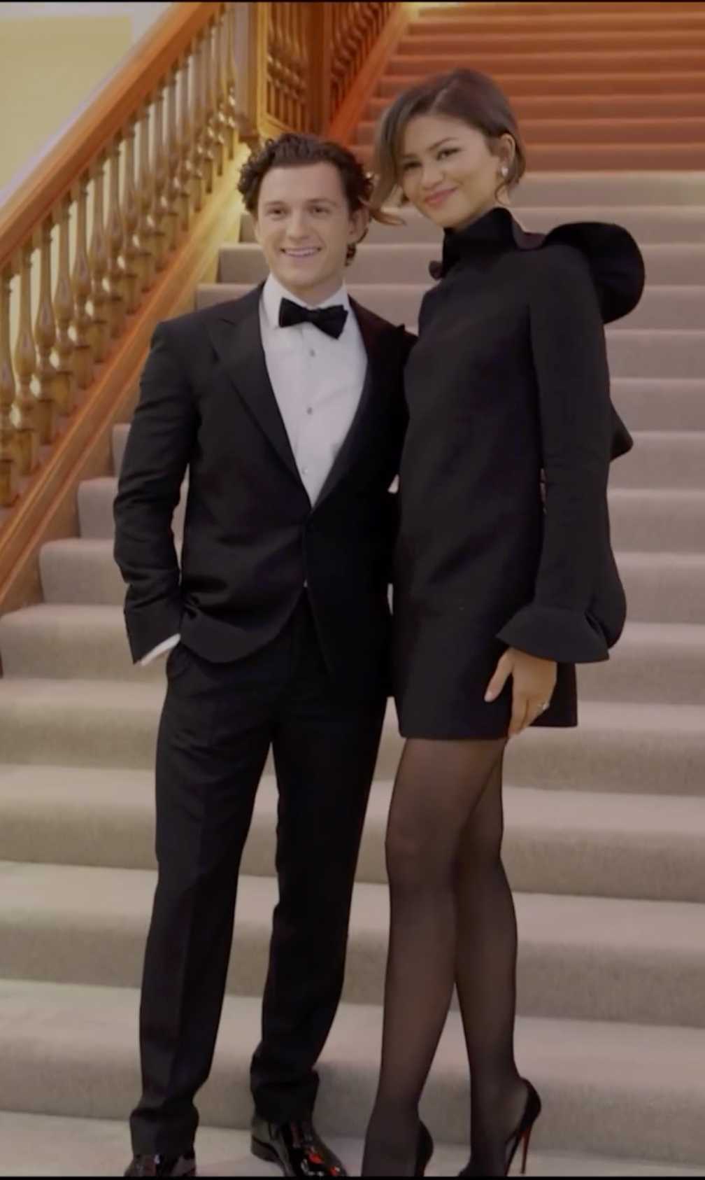 Tom Holland in a tuxedo and Zendaya in a black dress with a ring on her finger.