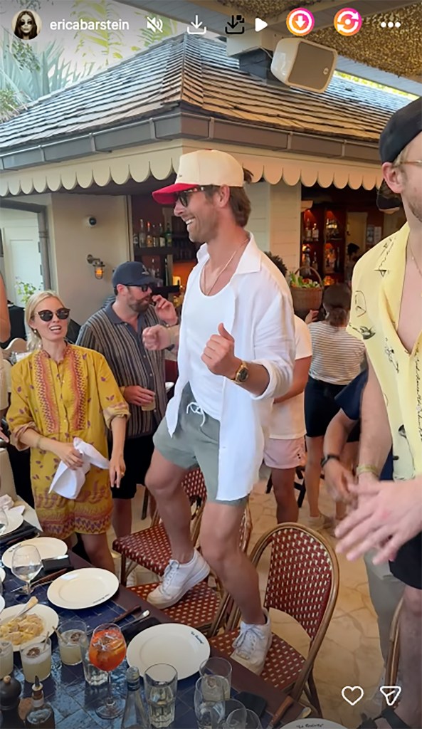 Glen Powell dancing on a chair at an outdoor restaurant.