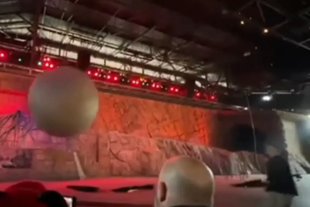 A large grey ball hanging in the air above a stage with a person visible.