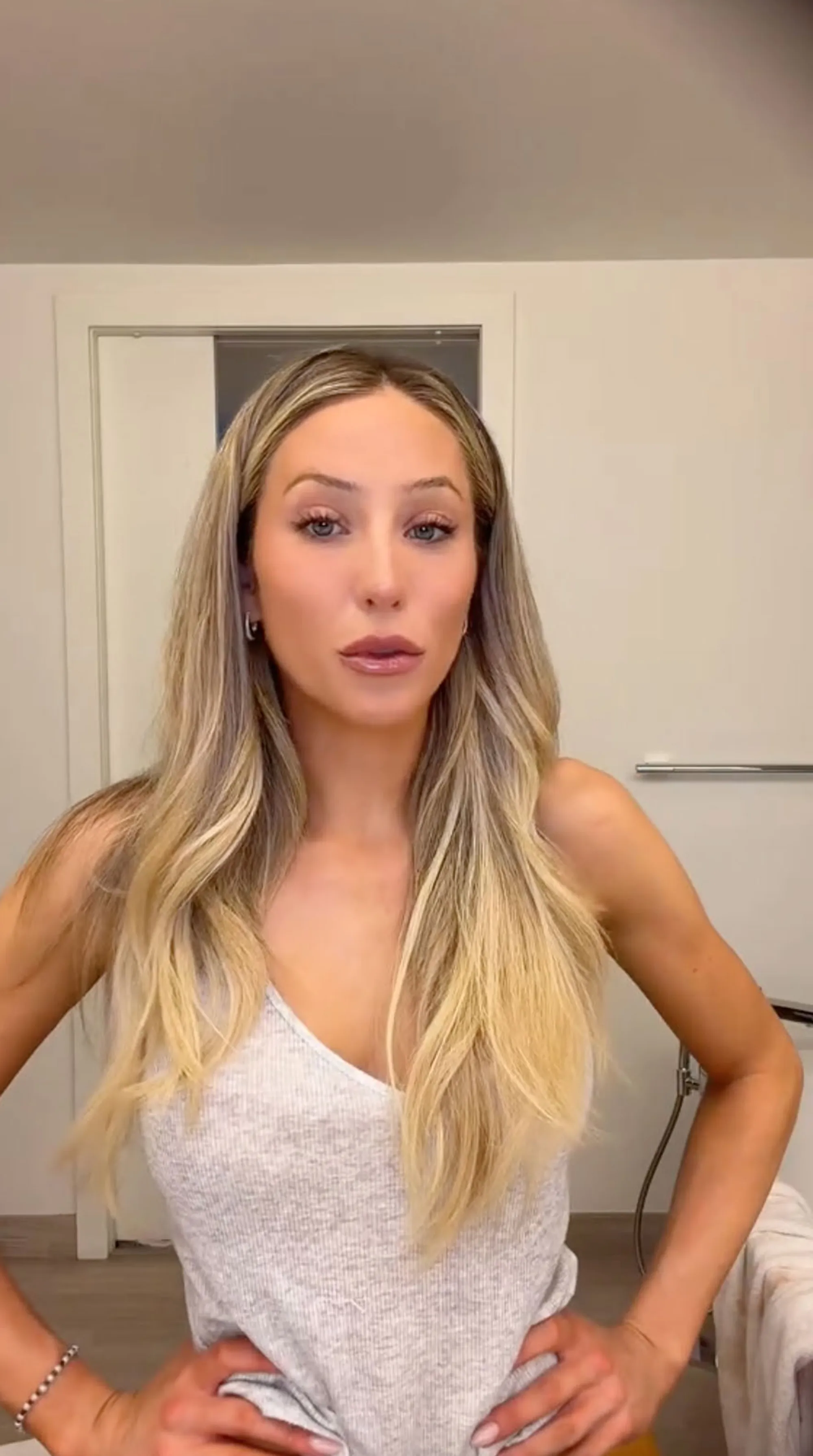 Alix Earle standing in a white tank top with hands on hips.